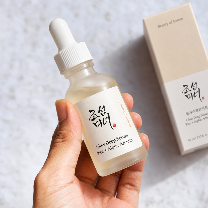 Beauty of Joseon Glow Deep Serum with Rice + Alpha-Arbutin held in a hand beside its matching beige box on a bright marble background