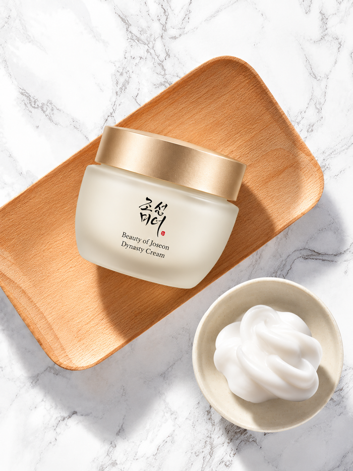 Beauty of Joseon Dynasty Cream jar on a warm wooden tray beside a bowl of white cream, styled on a bright marble surface with soft natural shadows.